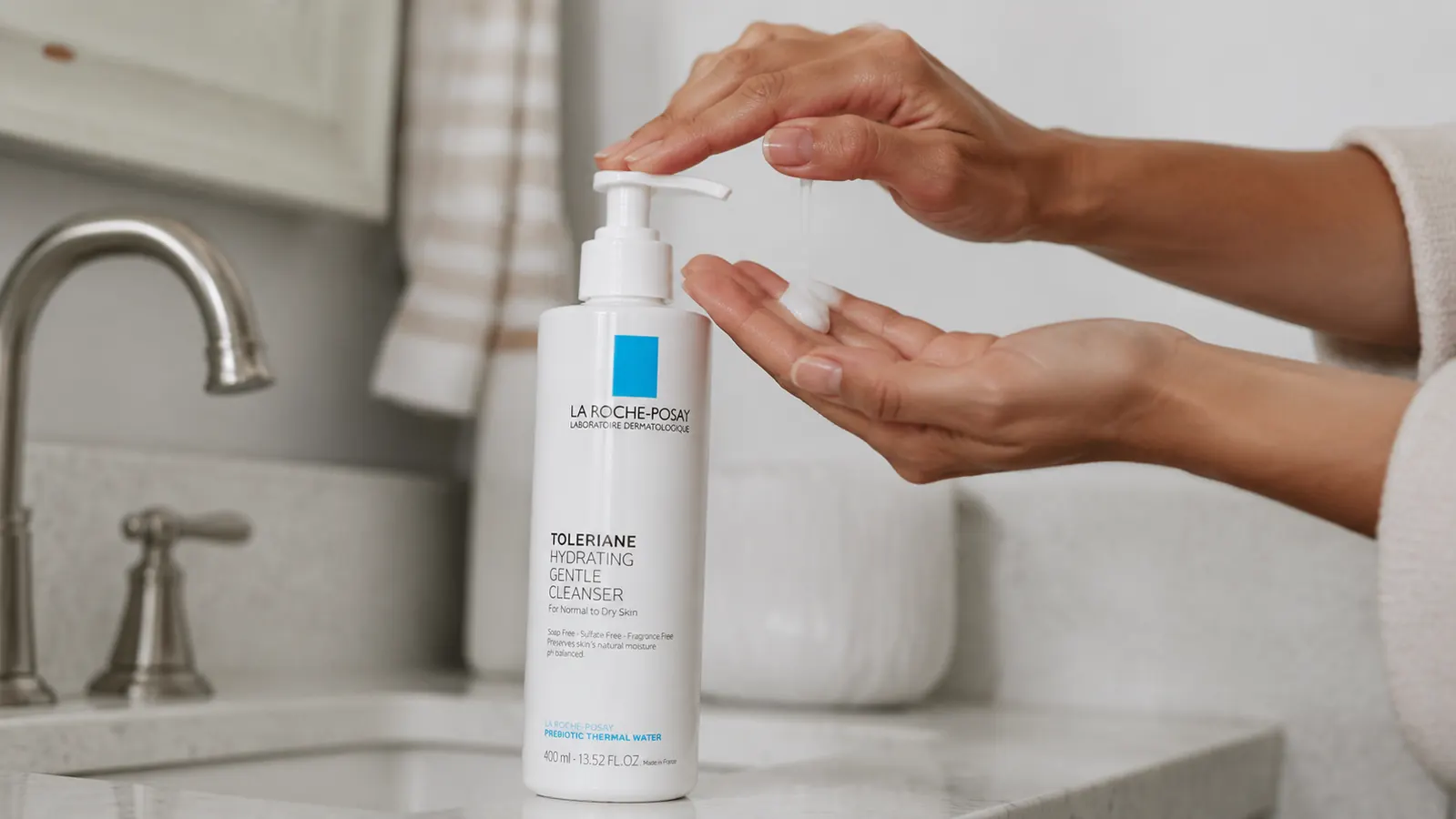 Hand squeezing a small amount of La Roche-Posay Toleriane cleanser onto fingertips over a sink