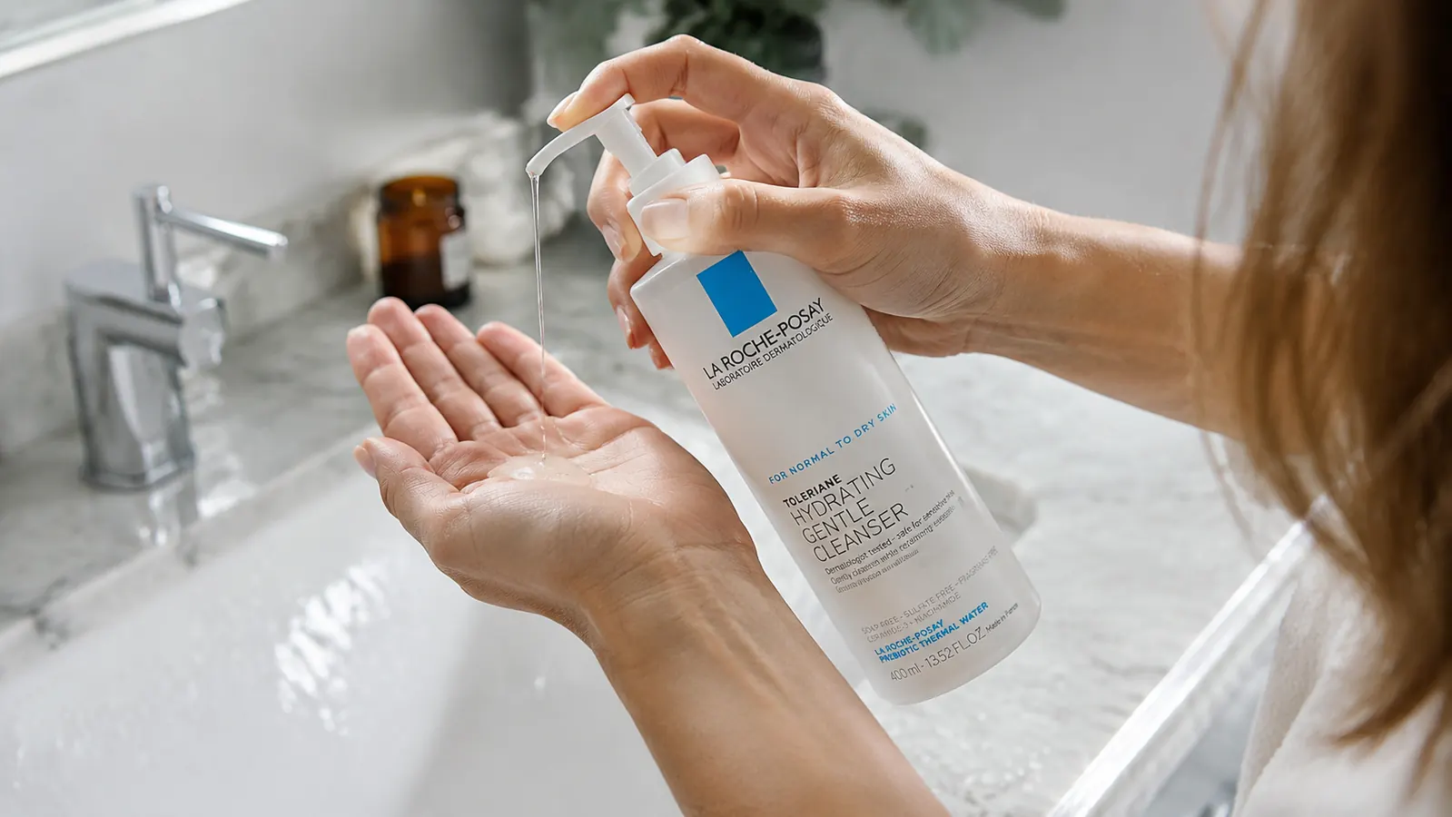 Hand dispensing La Roche-Posay Toleriane cleanser onto fingertips over a sink
