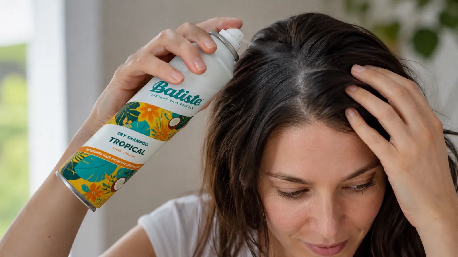 Hand holding a can of Batiste dry shampoo angled at the roots before spraying