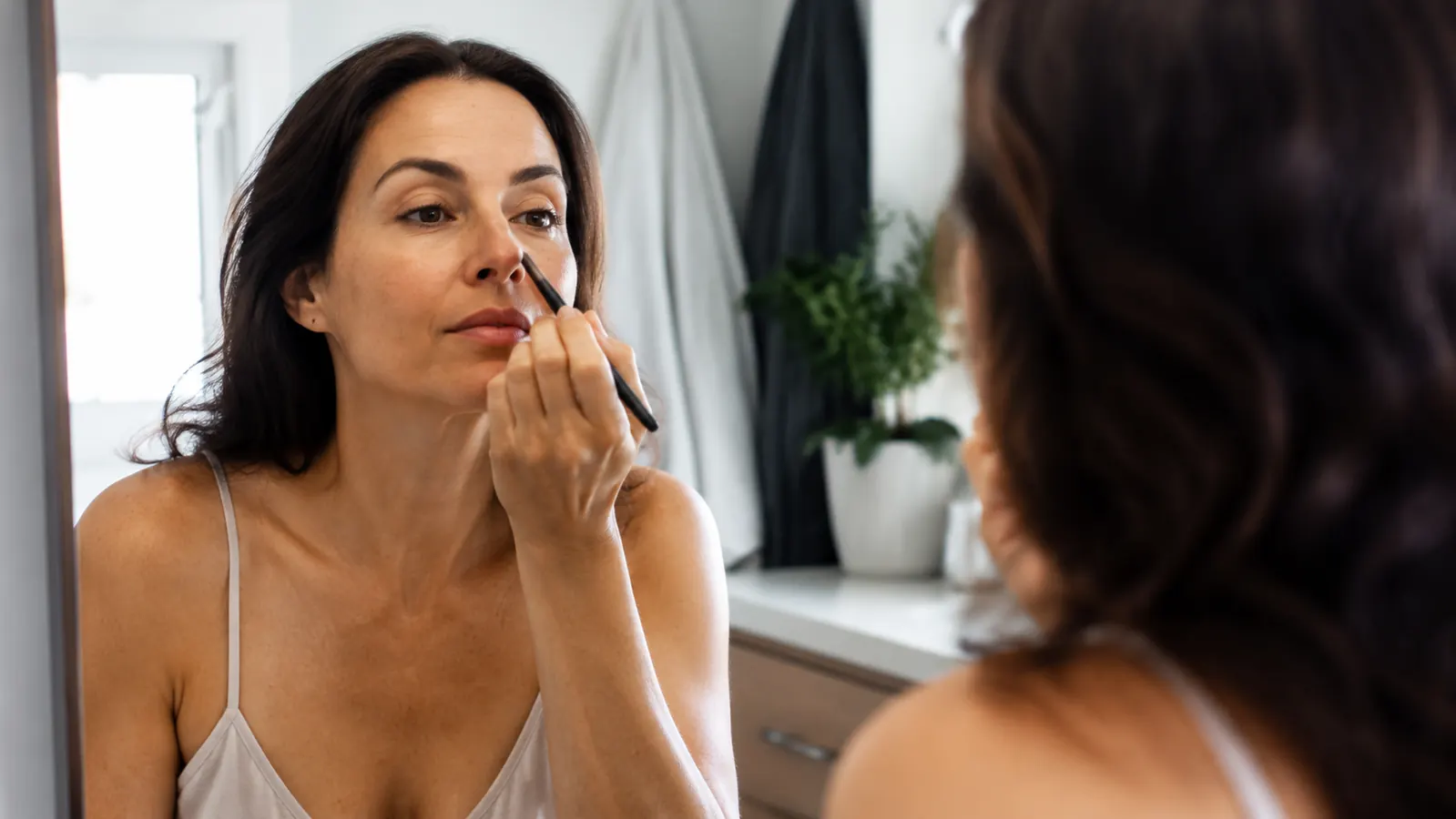 Woman applying mascara in natural light before heading out the door in the morning