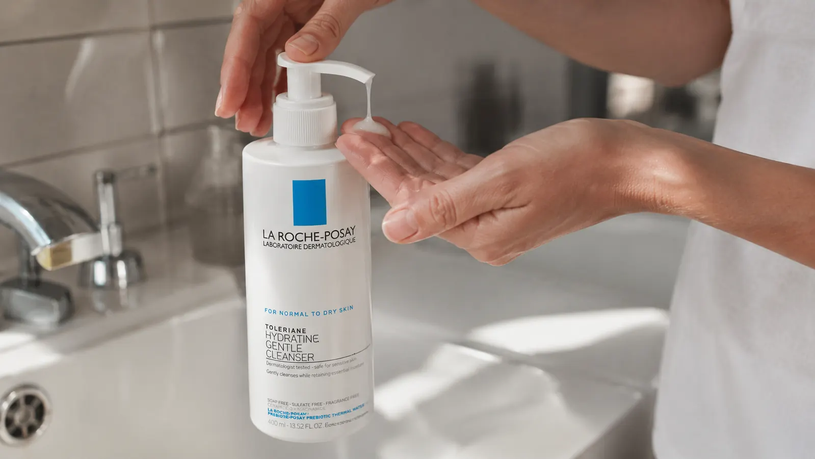 Hand squeezing La Roche-Posay Toleriane cleanser onto fingertips over a bathroom sink