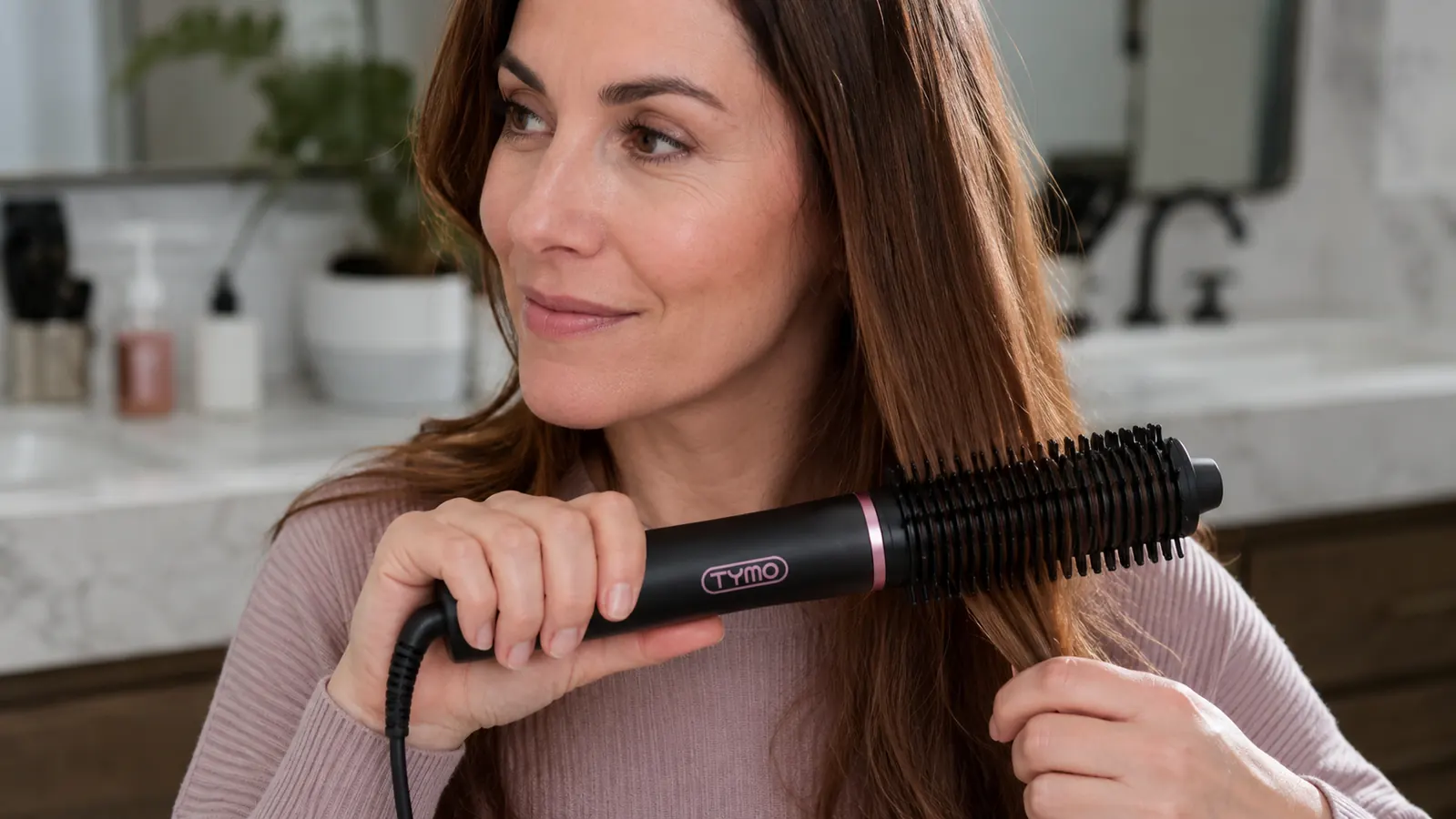 Hand holding the TYMO Ring straightener brush and pulling it through a section of hair near the ends