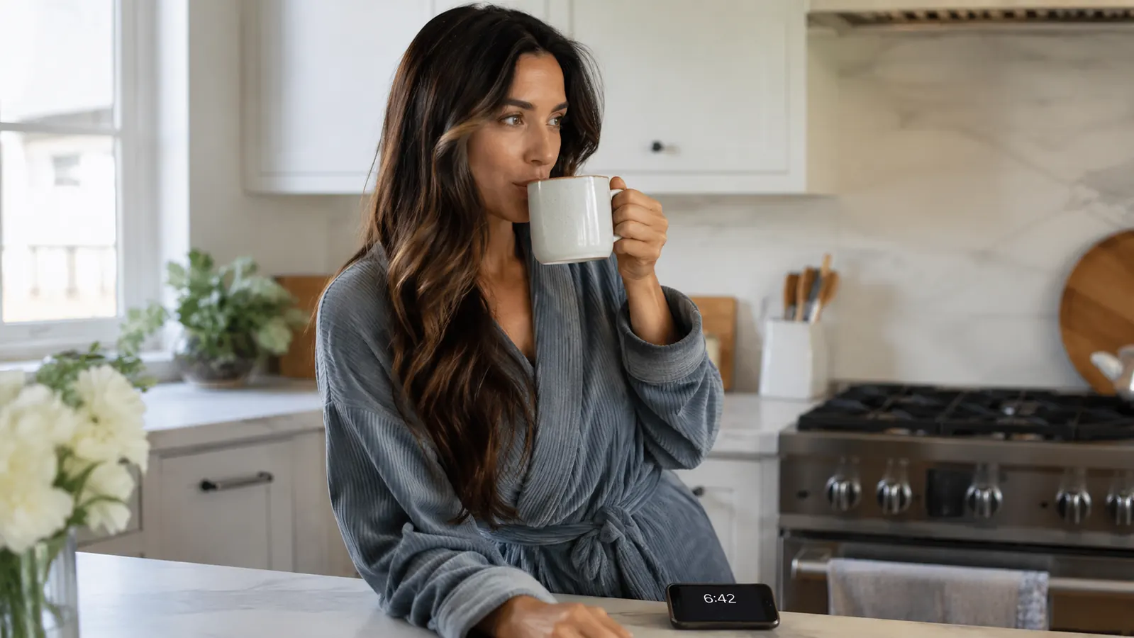Woman checking the time on her phone in the kitchen with her hair already done, coffee in hand, clearly ahead of schedule